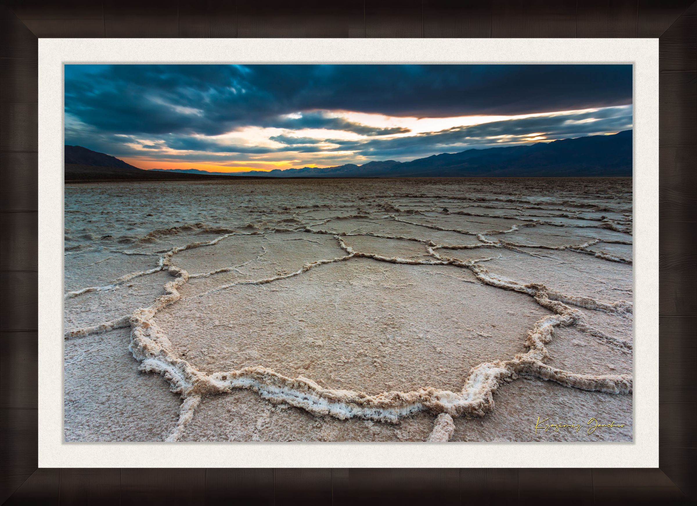 Expansive desert salt flat of Badwater Basin beneath a sky filled with storm clouds and setting sun in Death Valley. #Finish_Roma Dark Ash Frame & Bright Liner