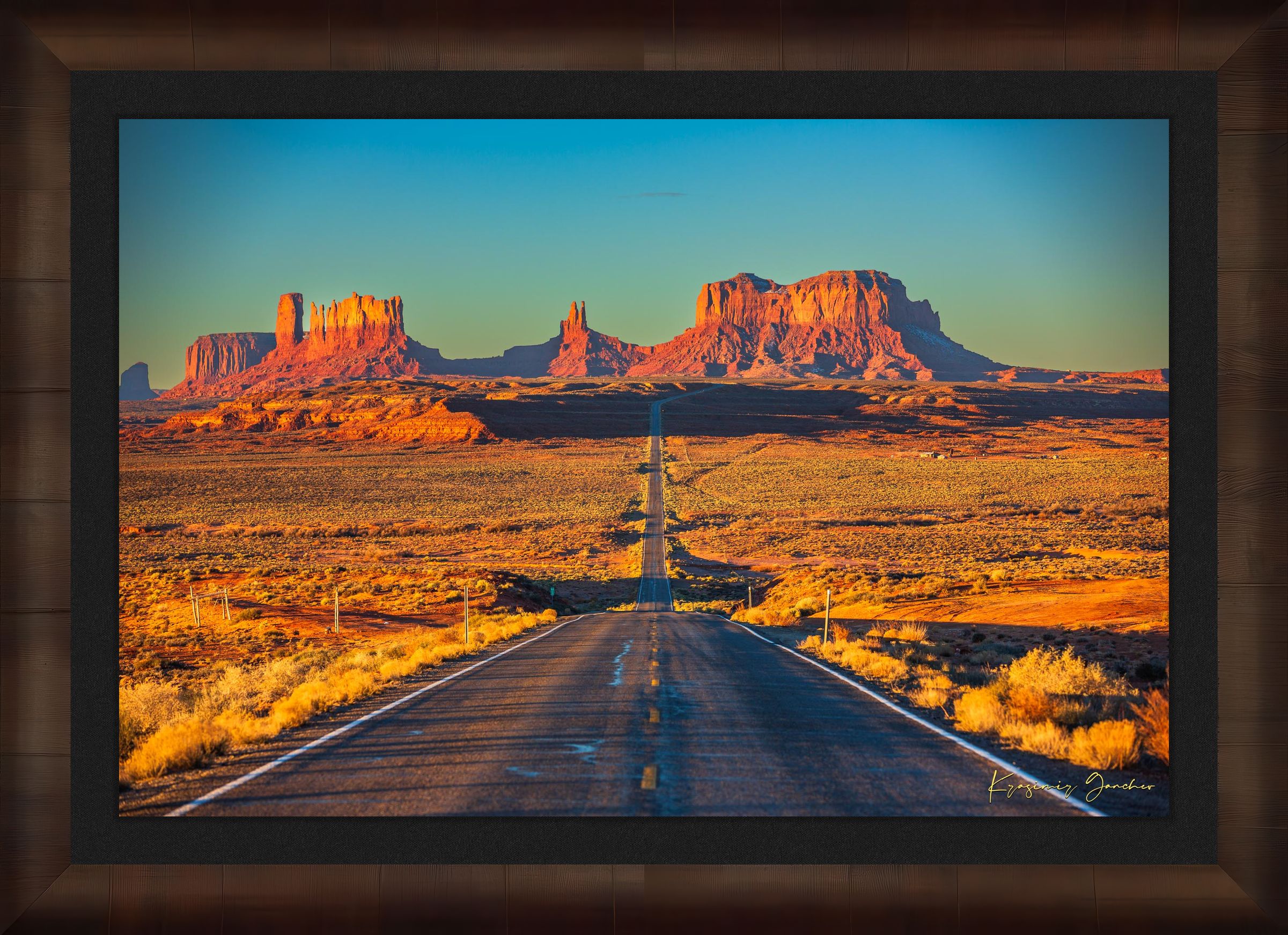 A winding road leads toward distant mesas under a hazy sky in Monument Valley, bathed in warm daylight and soft morning light. #Finish_Roma Cigar Leaf Frame & Dark Liner