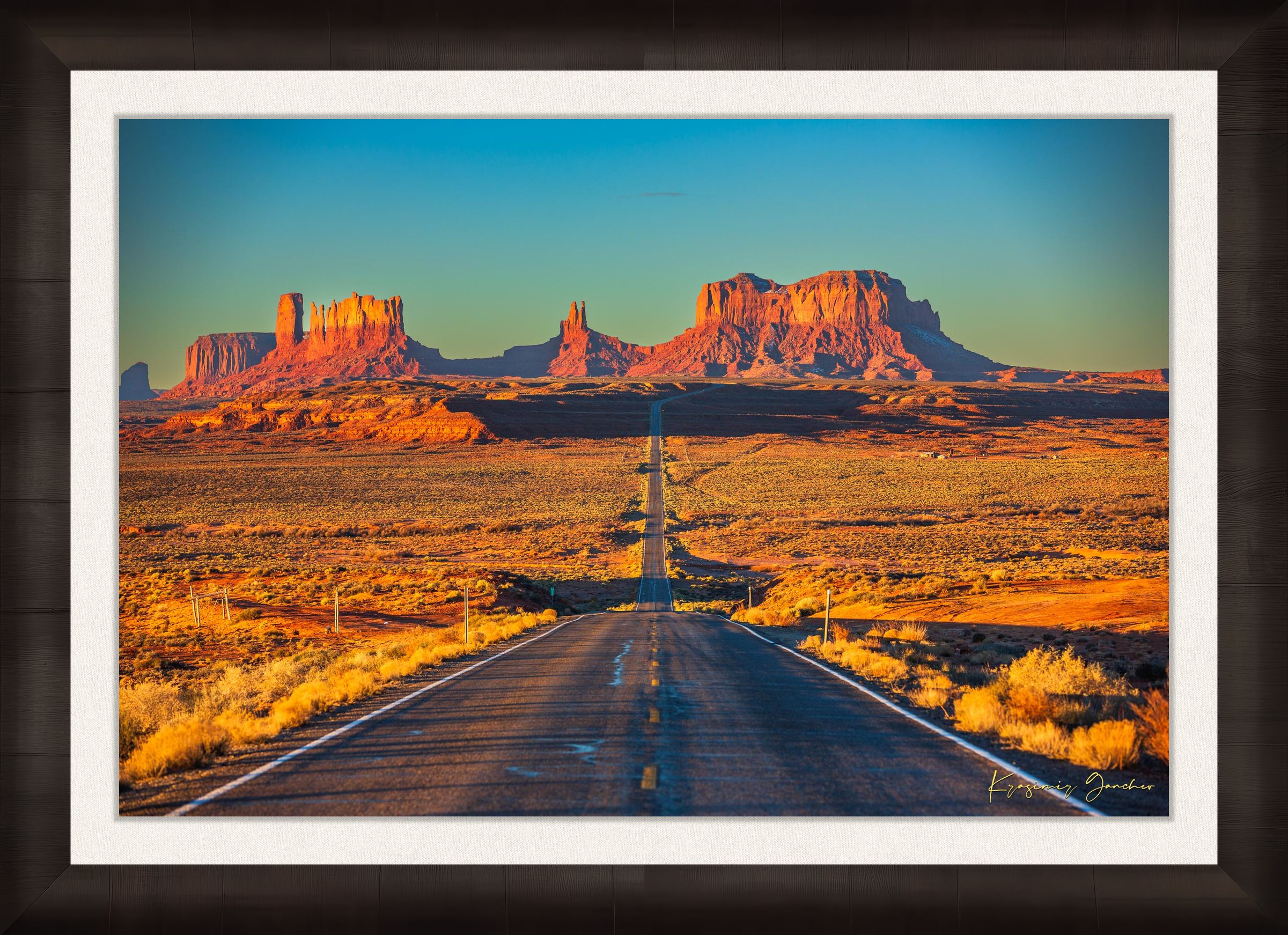 A winding road leads toward distant mesas under a hazy sky in Monument Valley, bathed in warm daylight and soft morning light. #Finish_Roma Dark Ash Frame & Bright Liner