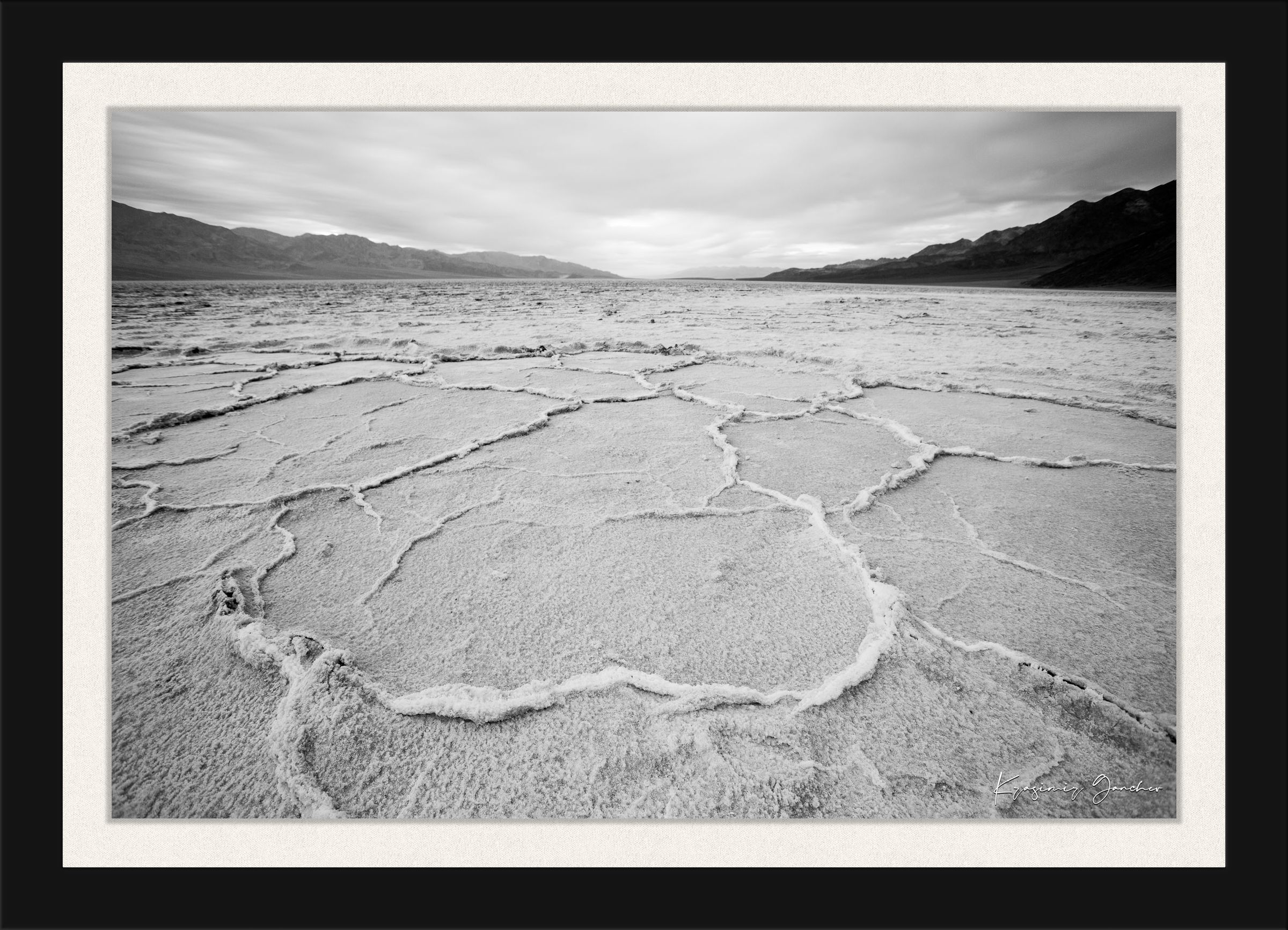 Cracked salt flat landscape in Death Valley National Park during sunset, showing textured surface under clear skies. #Finish_Roma Satin Black Frame & Bright Liner
