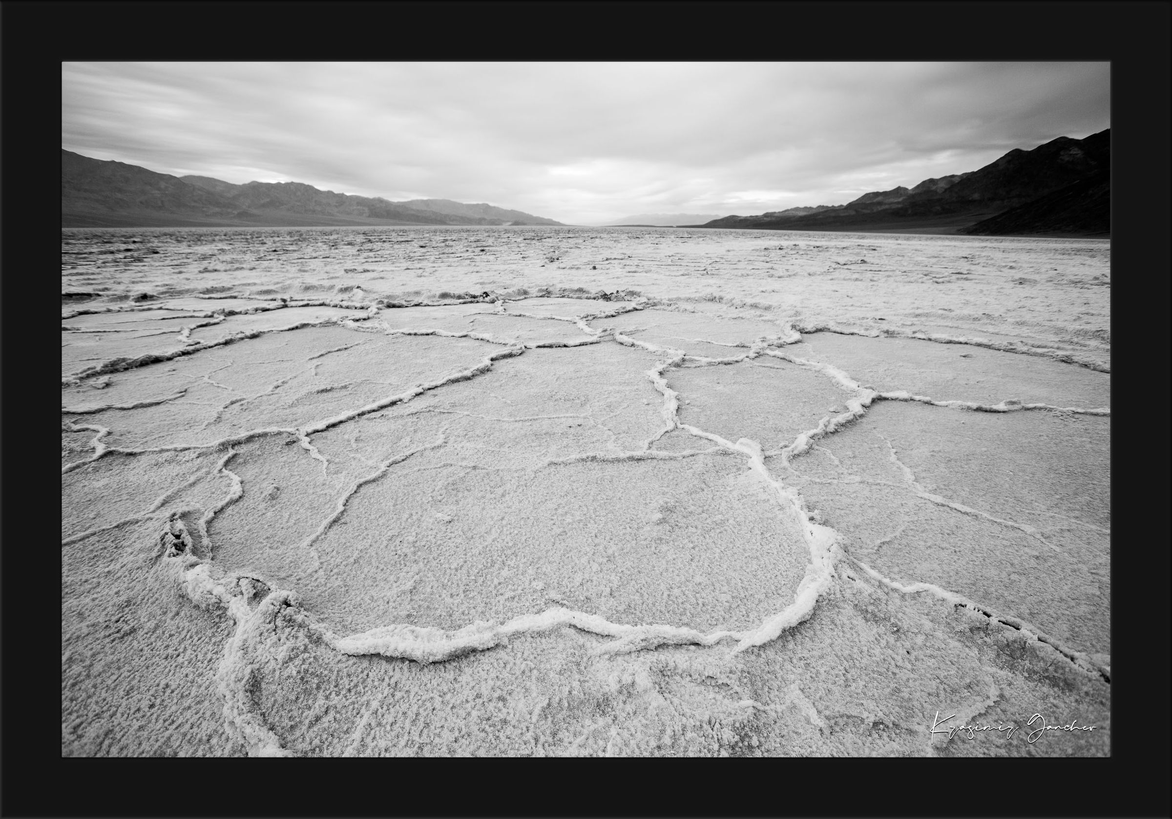 Cracked salt flat landscape in Death Valley National Park during sunset, showing textured surface under clear skies. #Finish_Roma Satin Black Frame