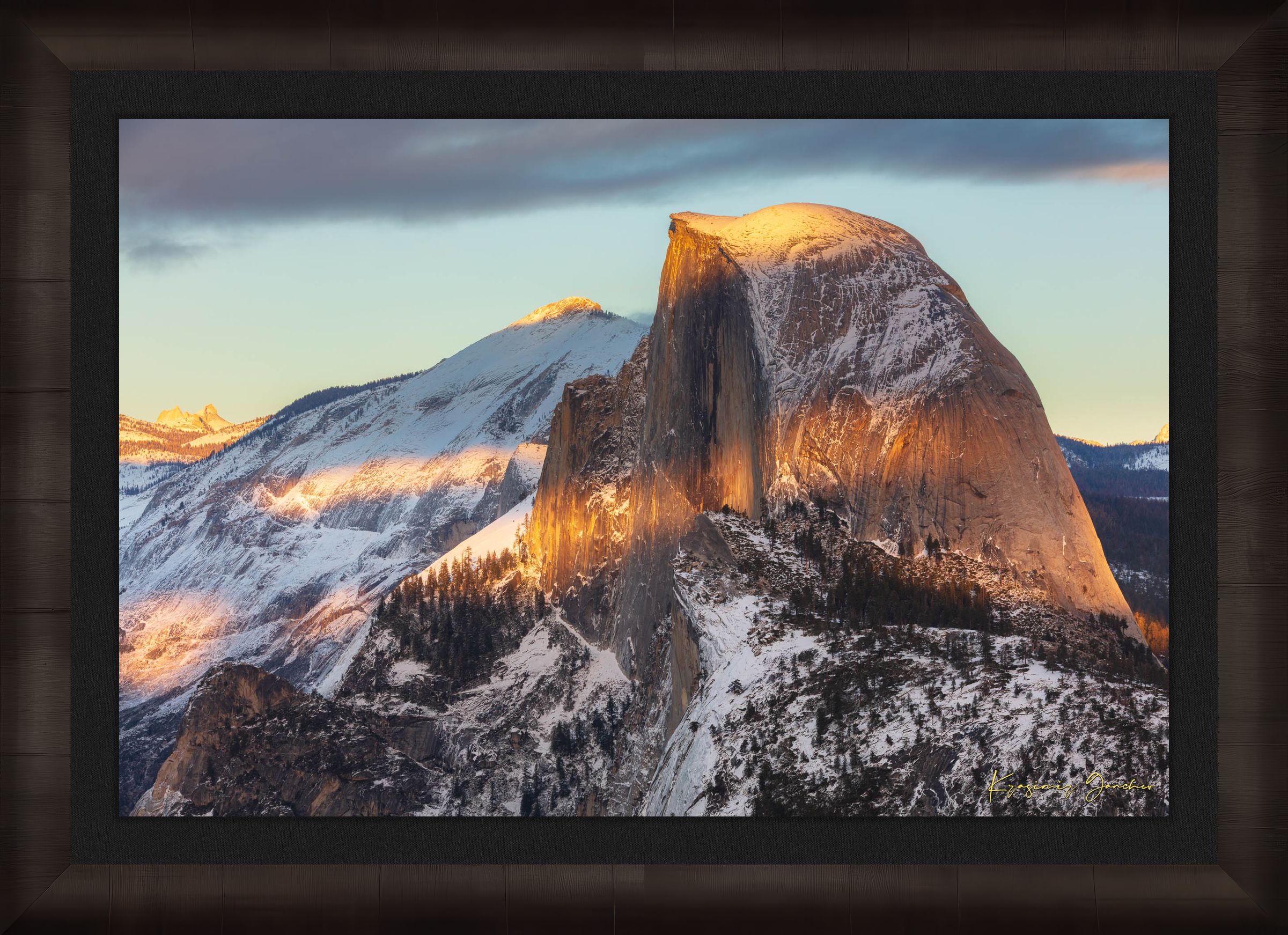 Half Dome monolith illuminated by golden sunset light amidst snow-covered peaks and clouds in Yosemite National Park. #Finish_Roma Dark Ash Frame & Dark Liner