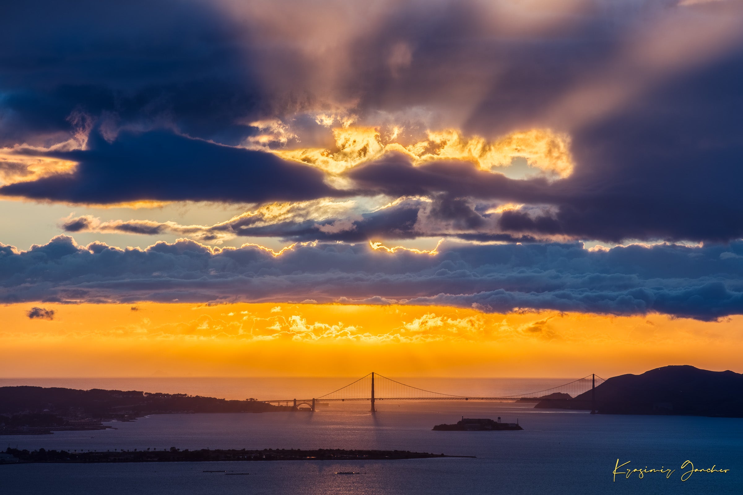 Golden Gate Bridge spanning a sunlit bay at sunset under layered stormy clouds, warm hues blending into cool sky tones. #Finish_Acrylic Recess