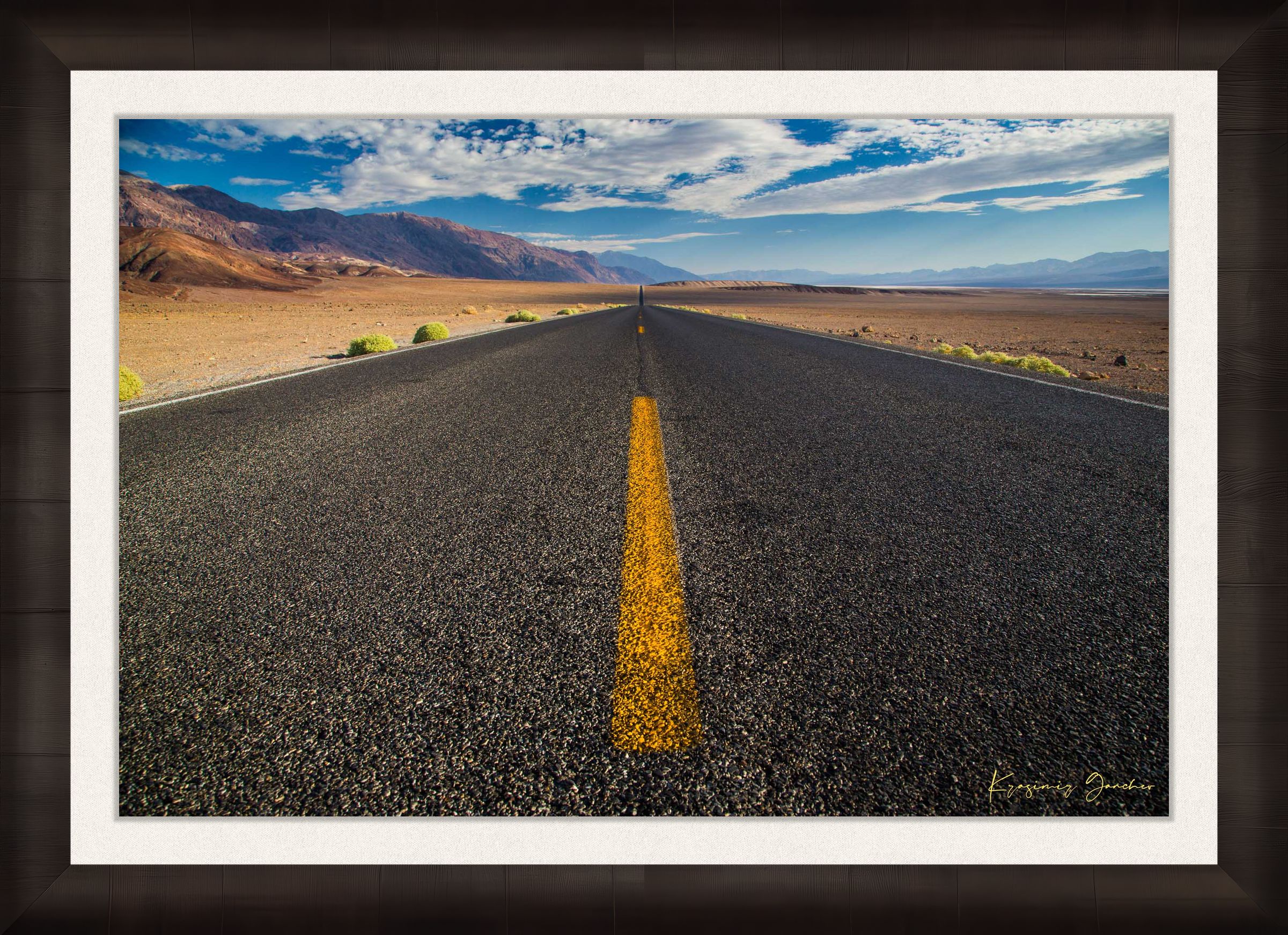 Straight desert road stretching into an open landscape of arid terrain in Death Valley National Park under overcast skies. #Finish_Roma Dark Ash Frame & Bright Liner