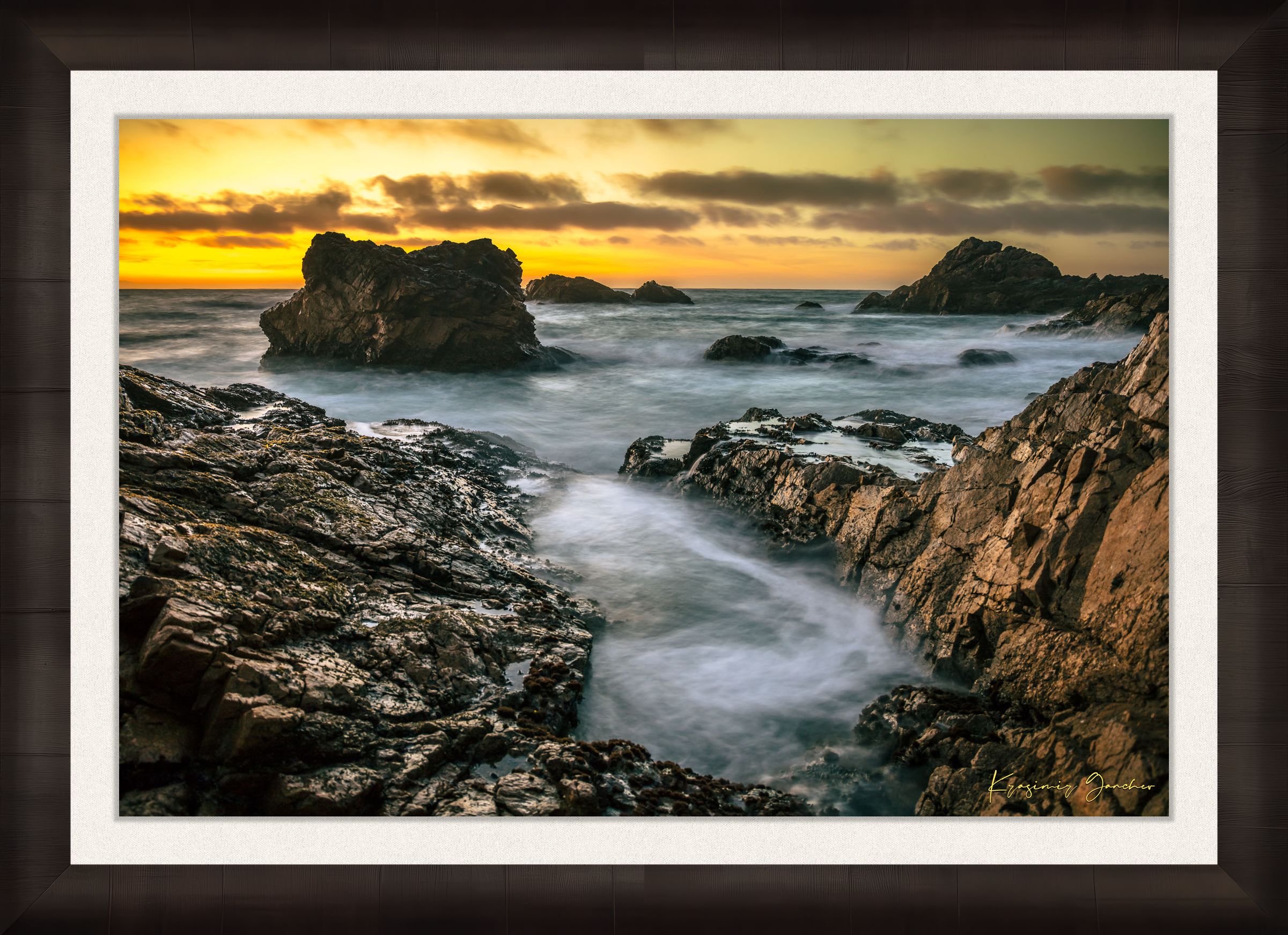 Jagged rocky cliffs along the Big Sur coast with rhythmic wave action, open ocean mist, clouds above, illuminated by late afternoon sunlight. #Finish_Roma Dark Ash Frame & Bright Liner