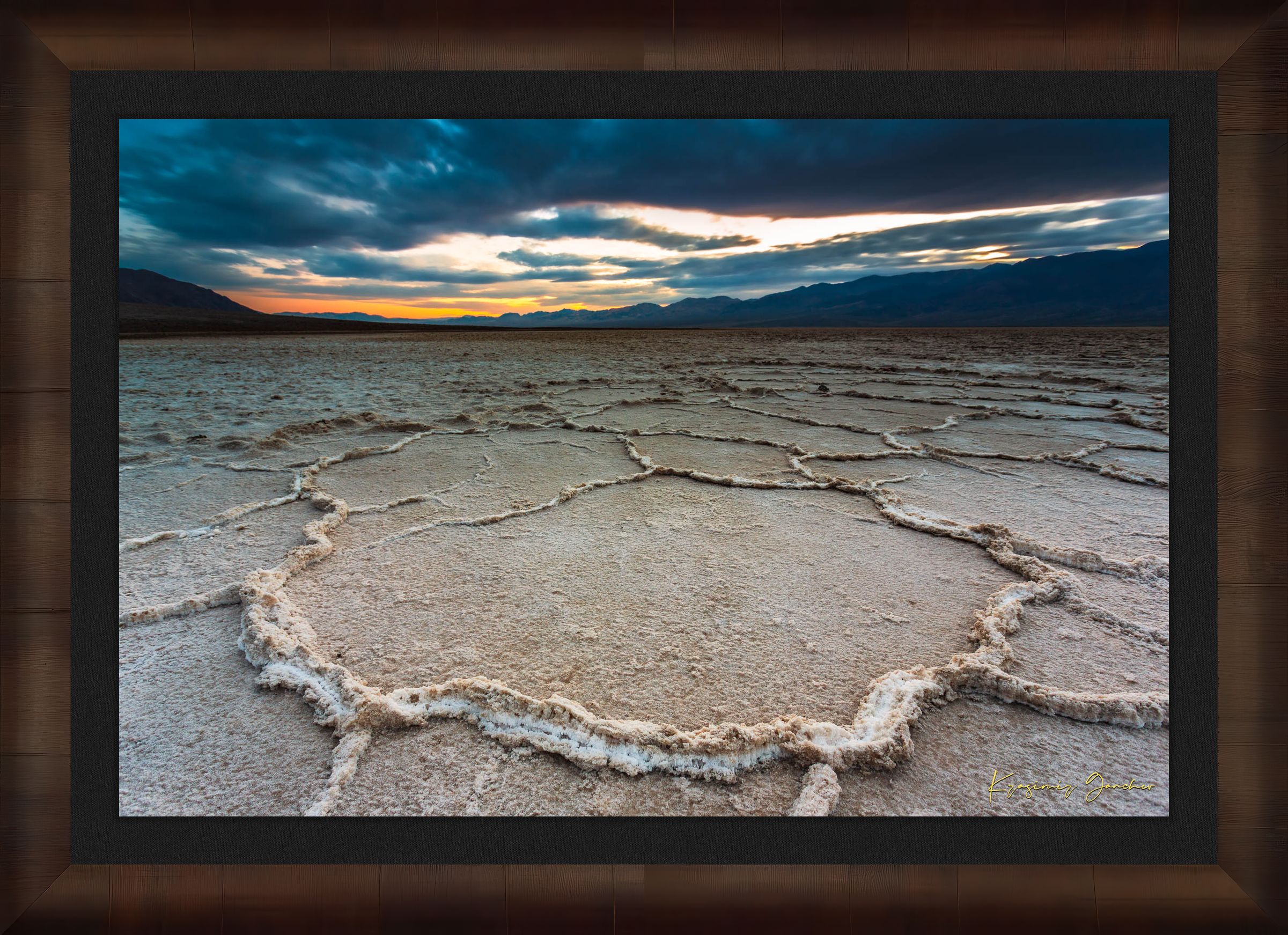 Expansive desert salt flat of Badwater Basin beneath a sky filled with storm clouds and setting sun in Death Valley. #Finish_Roma Cigar Leaf Frame & Dark Liner