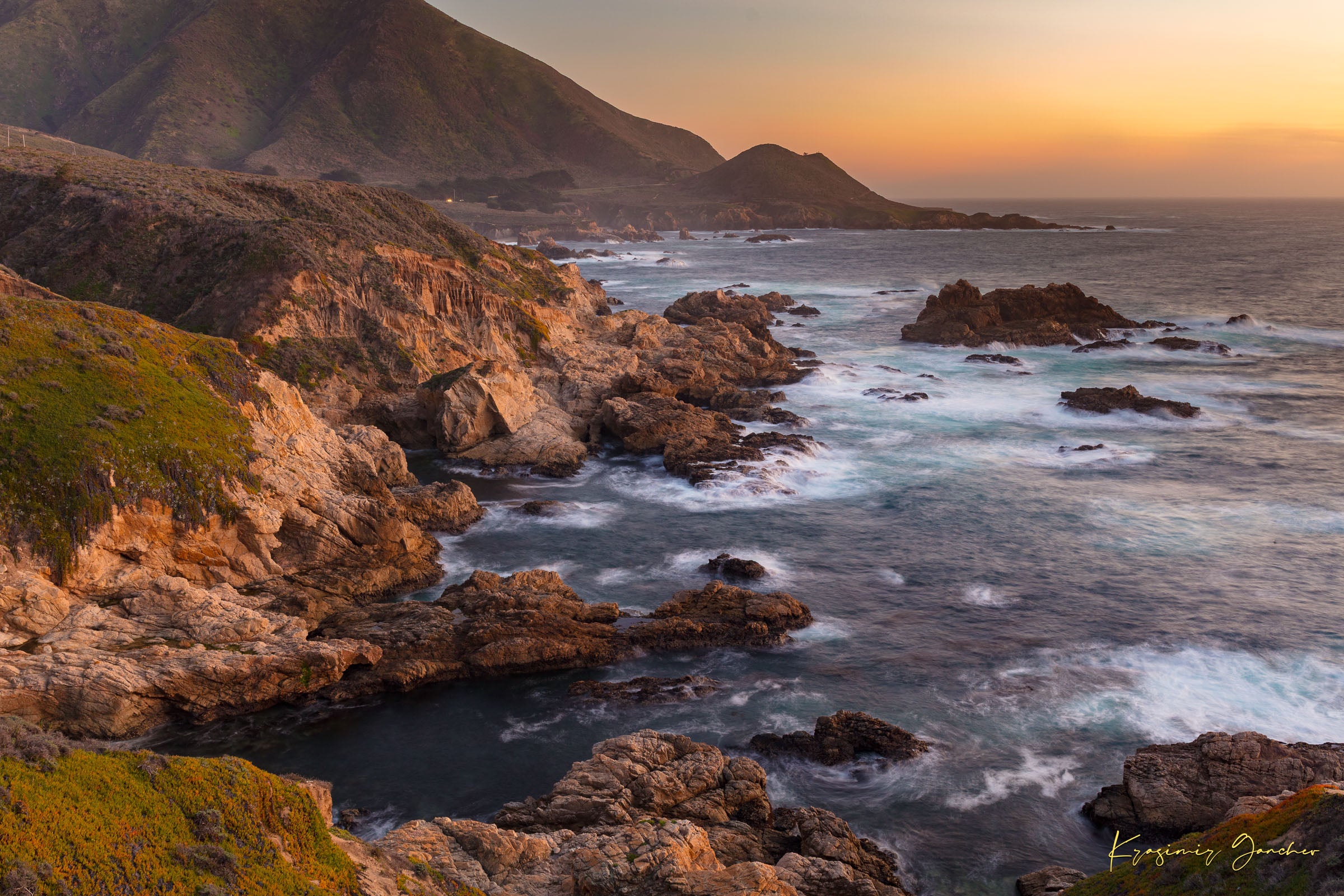 Rugged coastline of Big Sur featuring dark boulder formations, green slopes, ocean waves, and soft sunset glow across land and sea. #Finish_Acrylic Recess