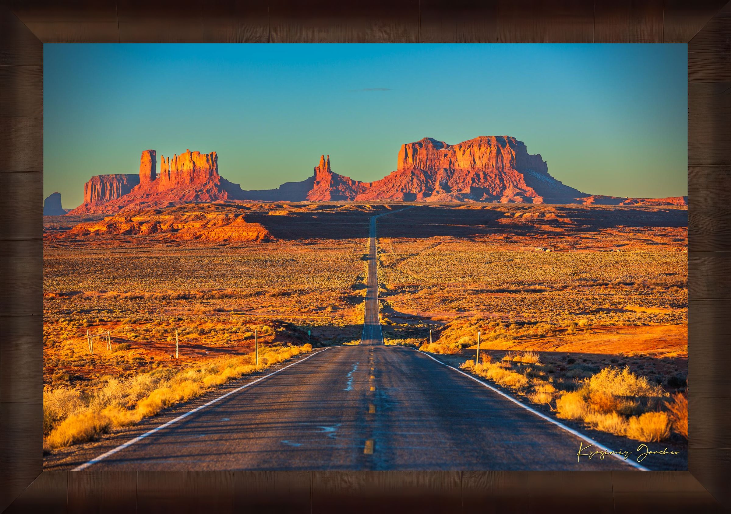 A winding road leads toward distant mesas under a hazy sky in Monument Valley, bathed in warm daylight and soft morning light. #Finish_Roma Cigar Leaf Frame