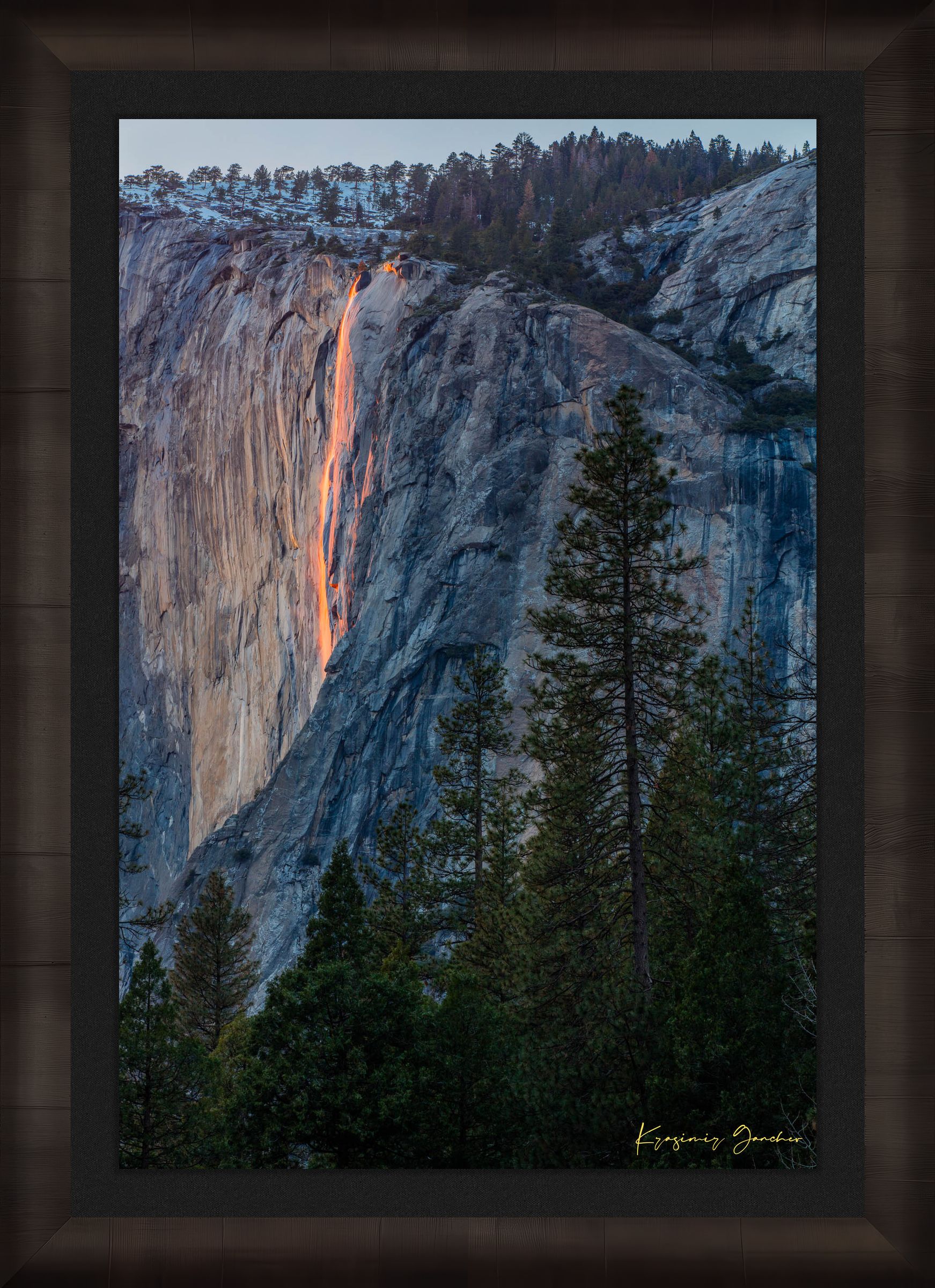 Firefall illuminated waterfall cascading on El Capitan monolith with foreground trees framing the scene during a cloudy sunset in Yosemite. #Finish_Roma Dark Ash Frame & Dark Liner