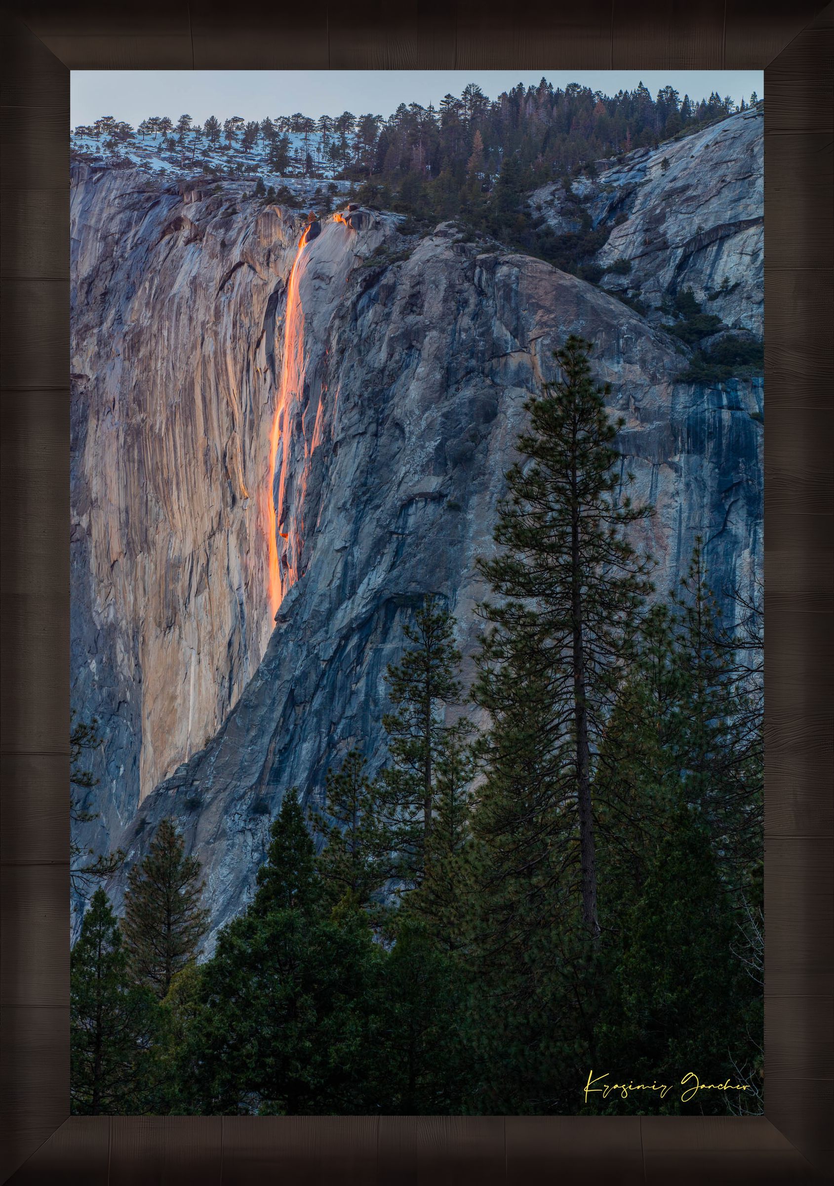 Firefall illuminated waterfall cascading on El Capitan monolith with foreground trees framing the scene during a cloudy sunset in Yosemite. #Finish_Roma Dark Ash Frame
