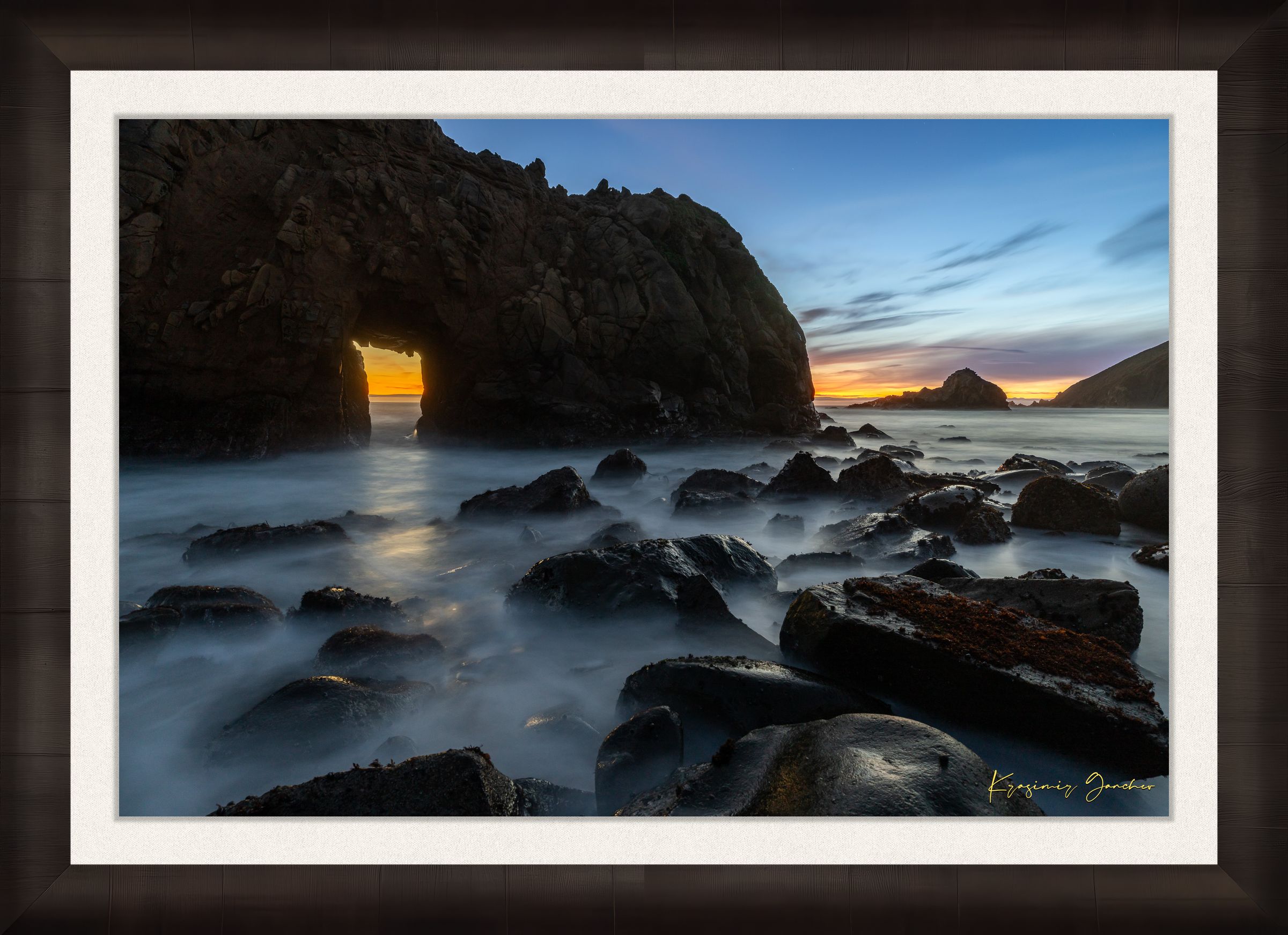 Natural arch structure with boulders and sea stack near Big Sur, California, lit by intense sunset rays through a stone opening. #Finish_Roma Dark Ash Frame & Bright Liner