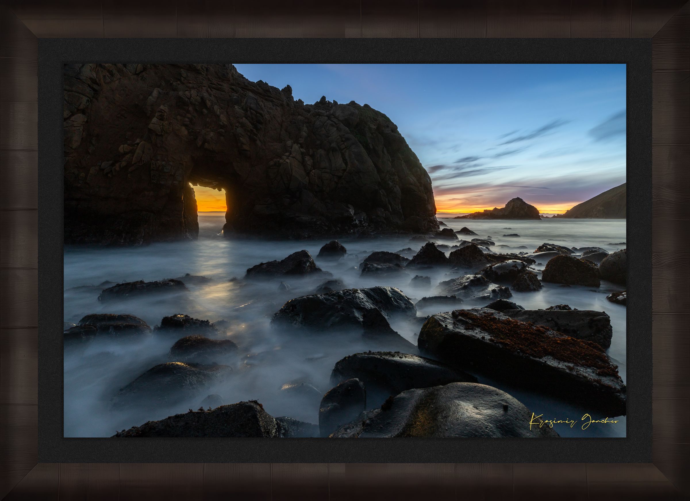 Natural arch structure with boulders and sea stack near Big Sur, California, lit by intense sunset rays through a stone opening. #Finish_Roma Dark Ash Frame & Dark Liner