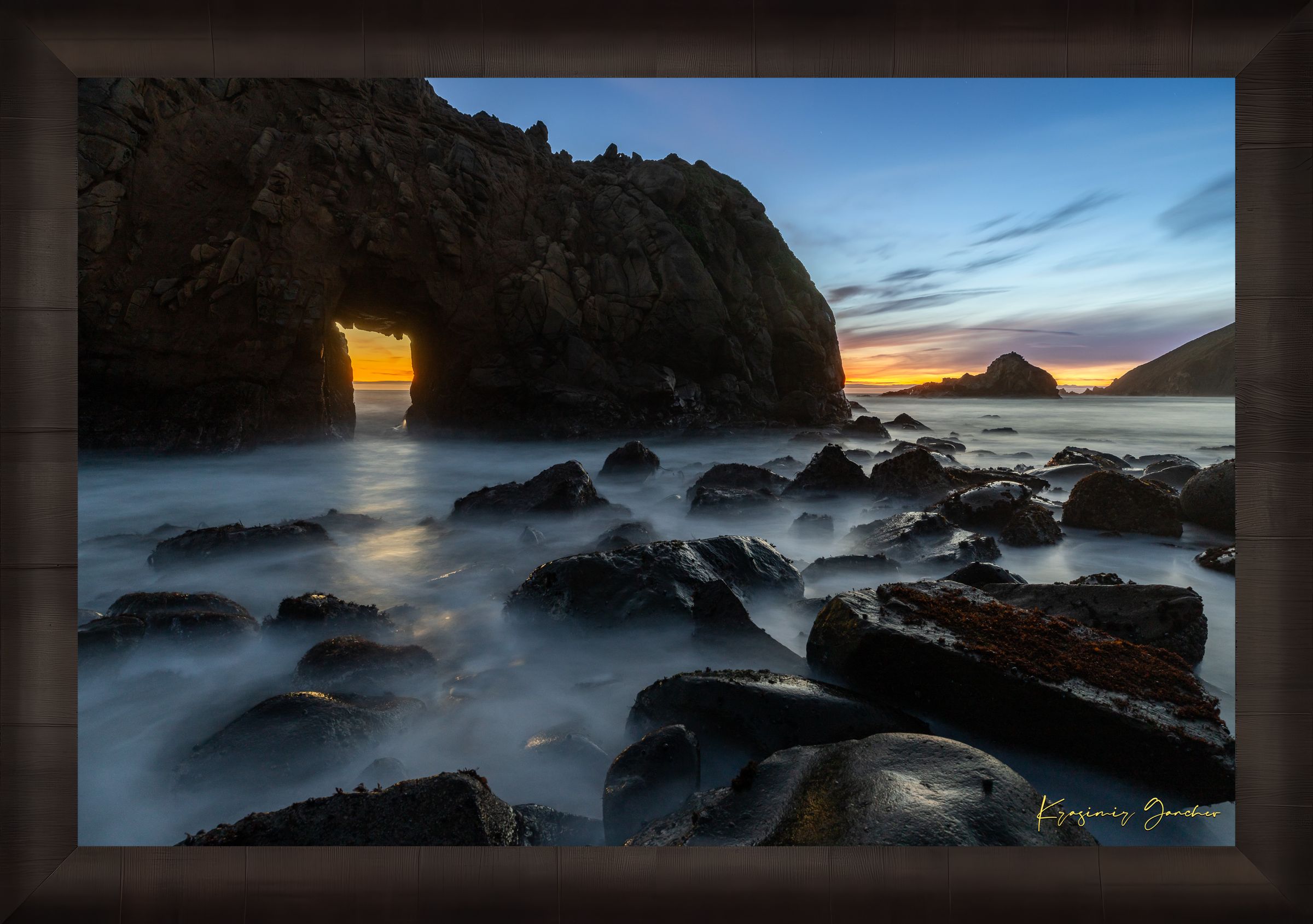Natural arch structure with boulders and sea stack near Big Sur, California, lit by intense sunset rays through a stone opening. #Finish_Roma Dark Ash Frame