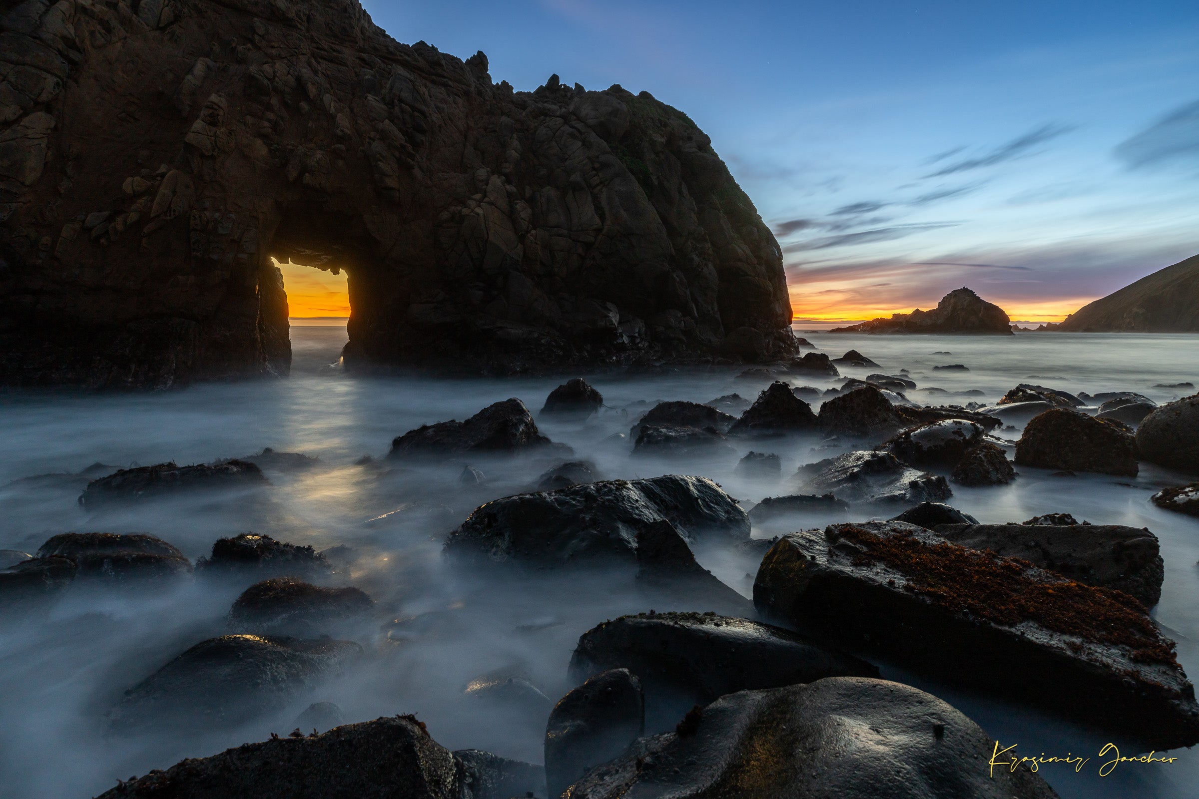 Natural arch structure with boulders and sea stack near Big Sur, California, lit by intense sunset rays through a stone opening. #Finish_Acrylic Recess