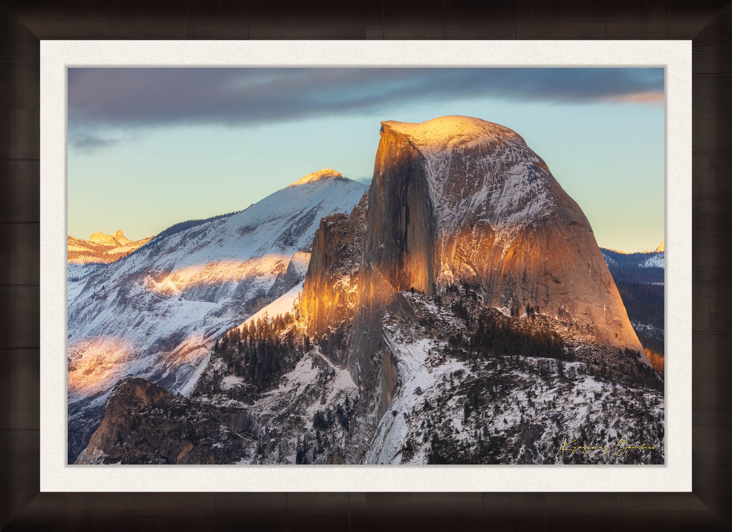 Half Dome monolith illuminated by golden sunset light amidst snow-covered peaks and clouds in Yosemite National Park. #Finish_Roma Dark Ash Frame & Bright Liner