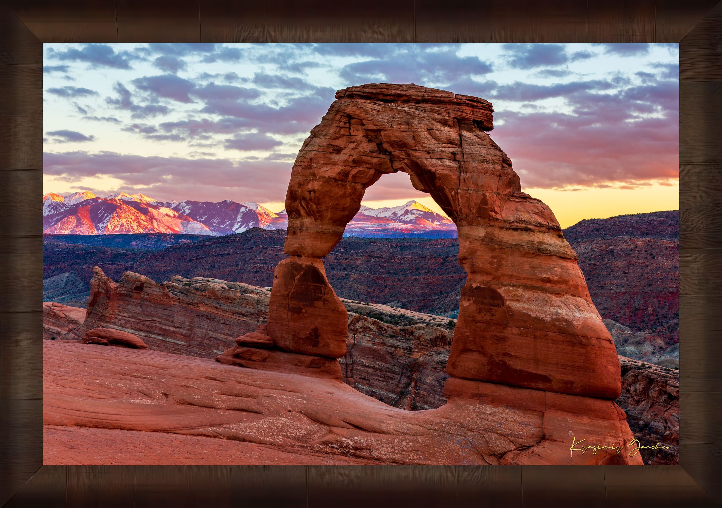 Natural arch of Delicate Arch in Arches National Park illuminated by sunset glow against a cloudy sky with vibrant reds and purples. #Finish_Roma Cigar Leaf Frame
