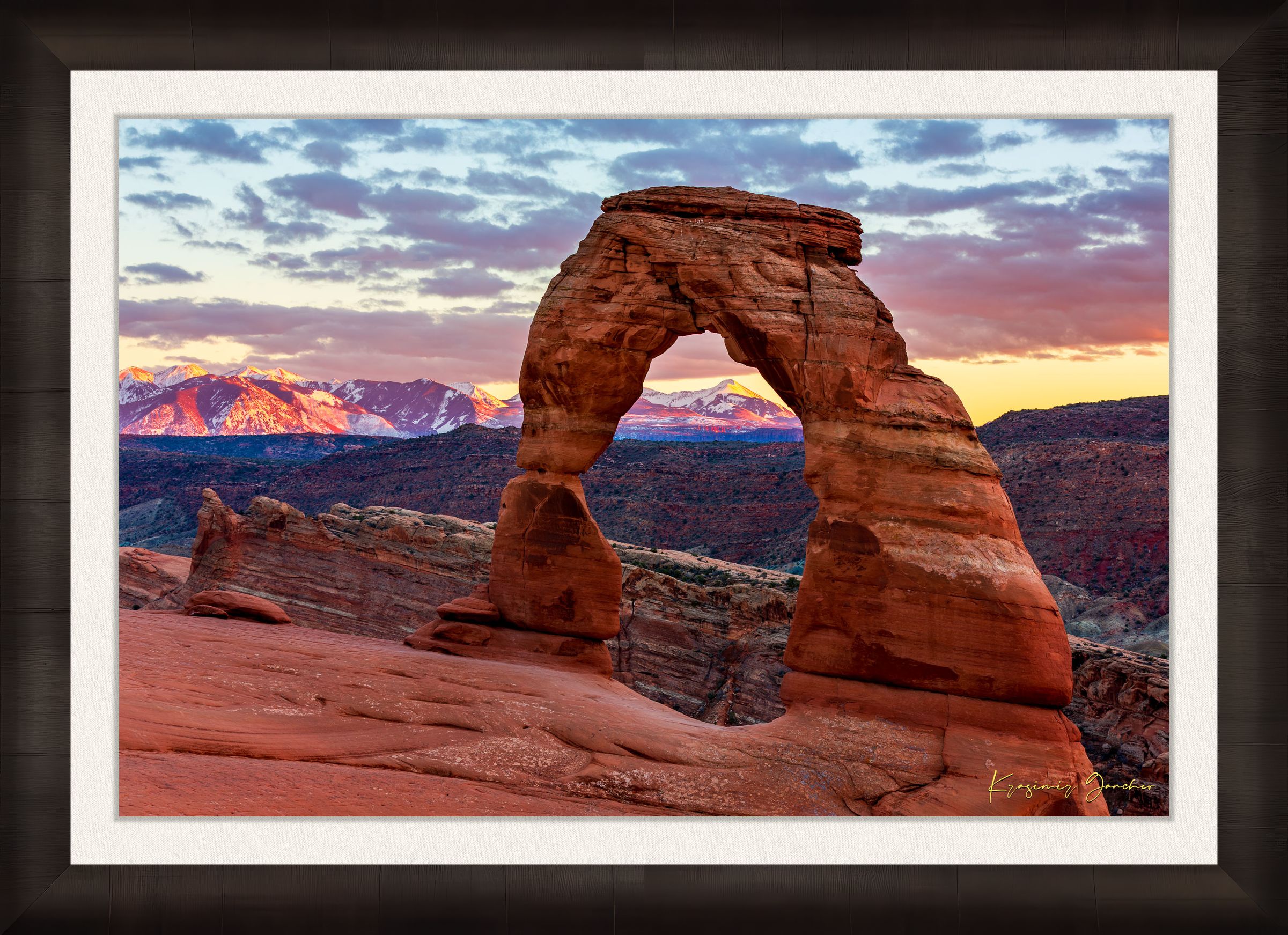Natural arch of Delicate Arch in Arches National Park illuminated by sunset glow against a cloudy sky with vibrant reds and purples. #Finish_Roma Dark Ash Frame & Bright Liner