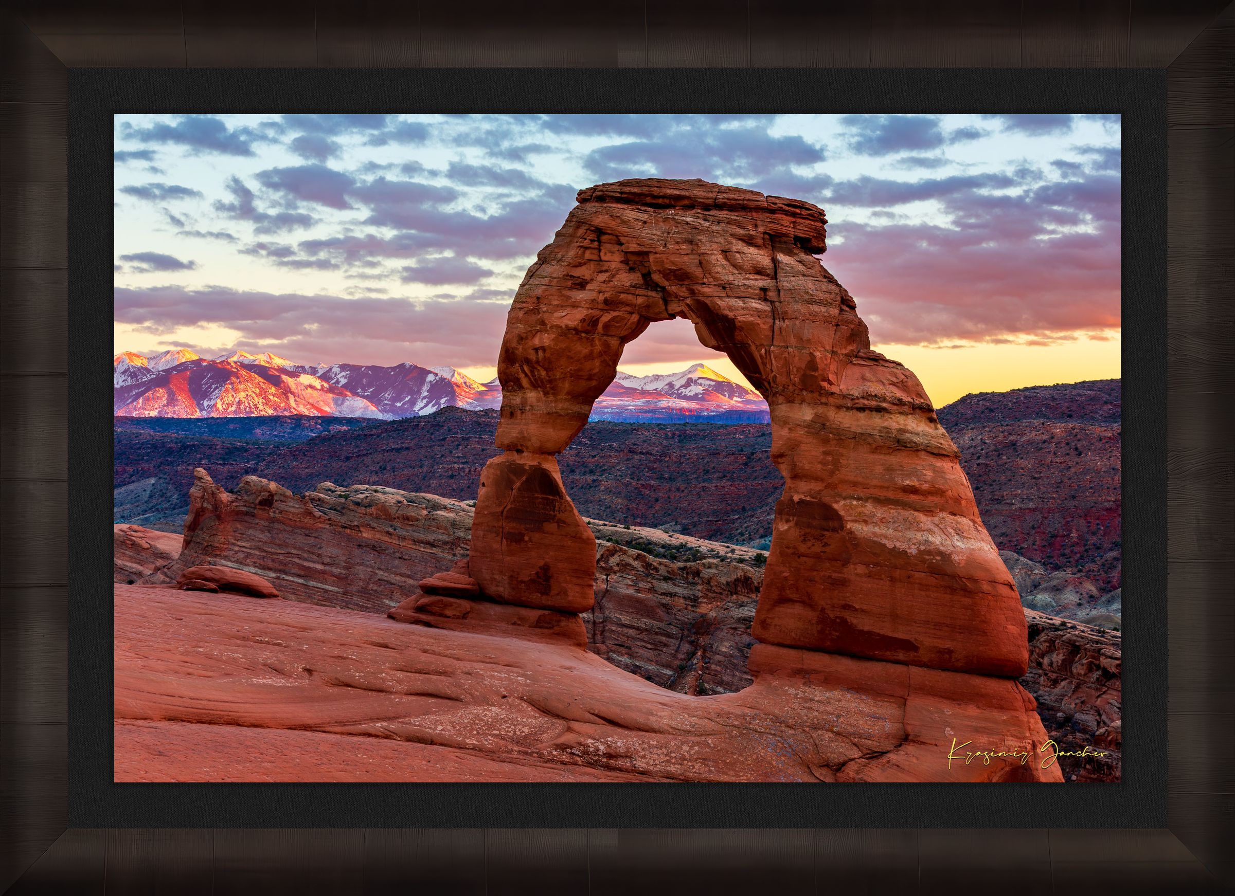 Natural arch of Delicate Arch in Arches National Park illuminated by sunset glow against a cloudy sky with vibrant reds and purples. #Finish_Roma Dark Ash Frame & Dark Liner