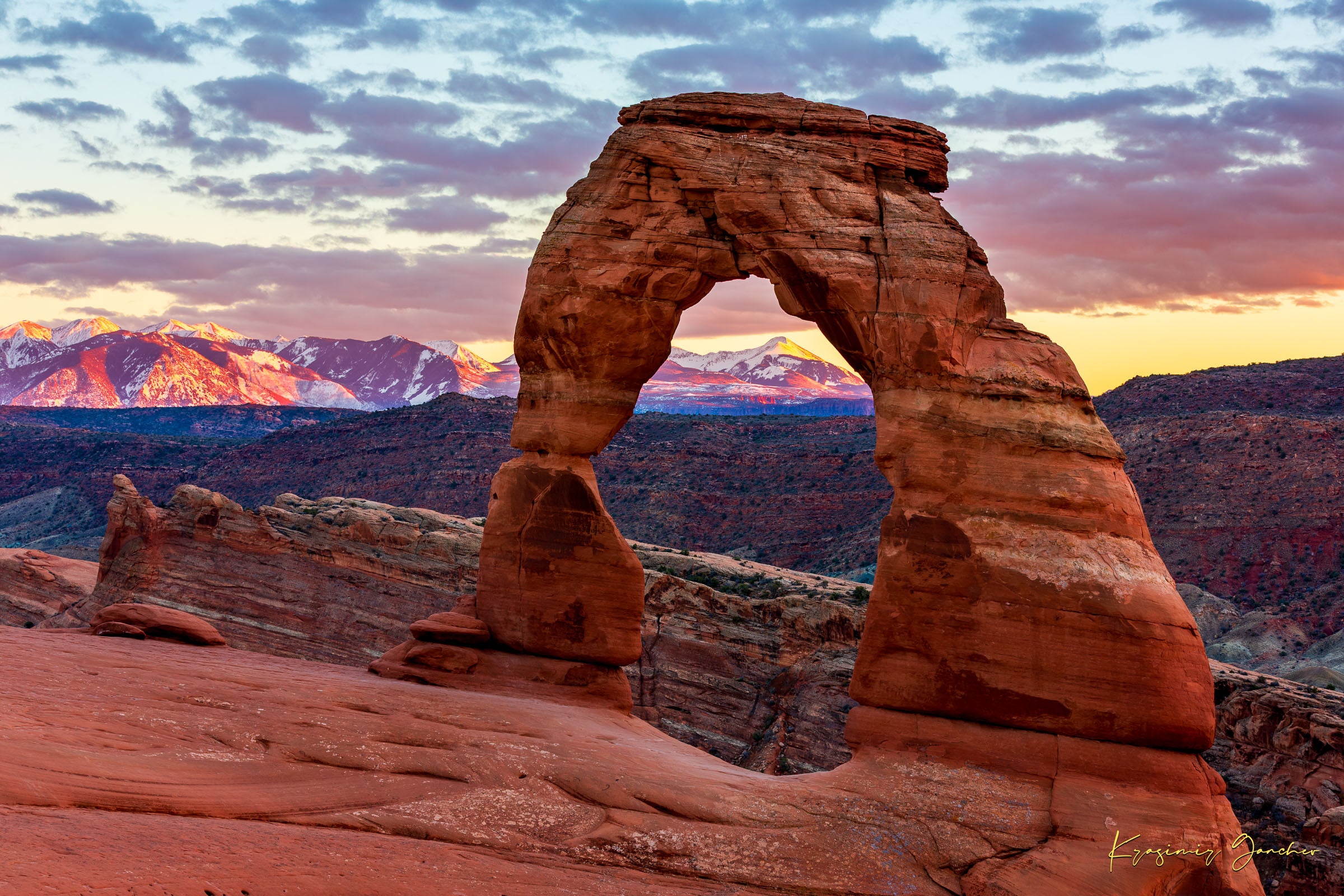 Natural arch of Delicate Arch in Arches National Park illuminated by sunset glow against a cloudy sky with vibrant reds and purples. #Finish_Acrylic Recess