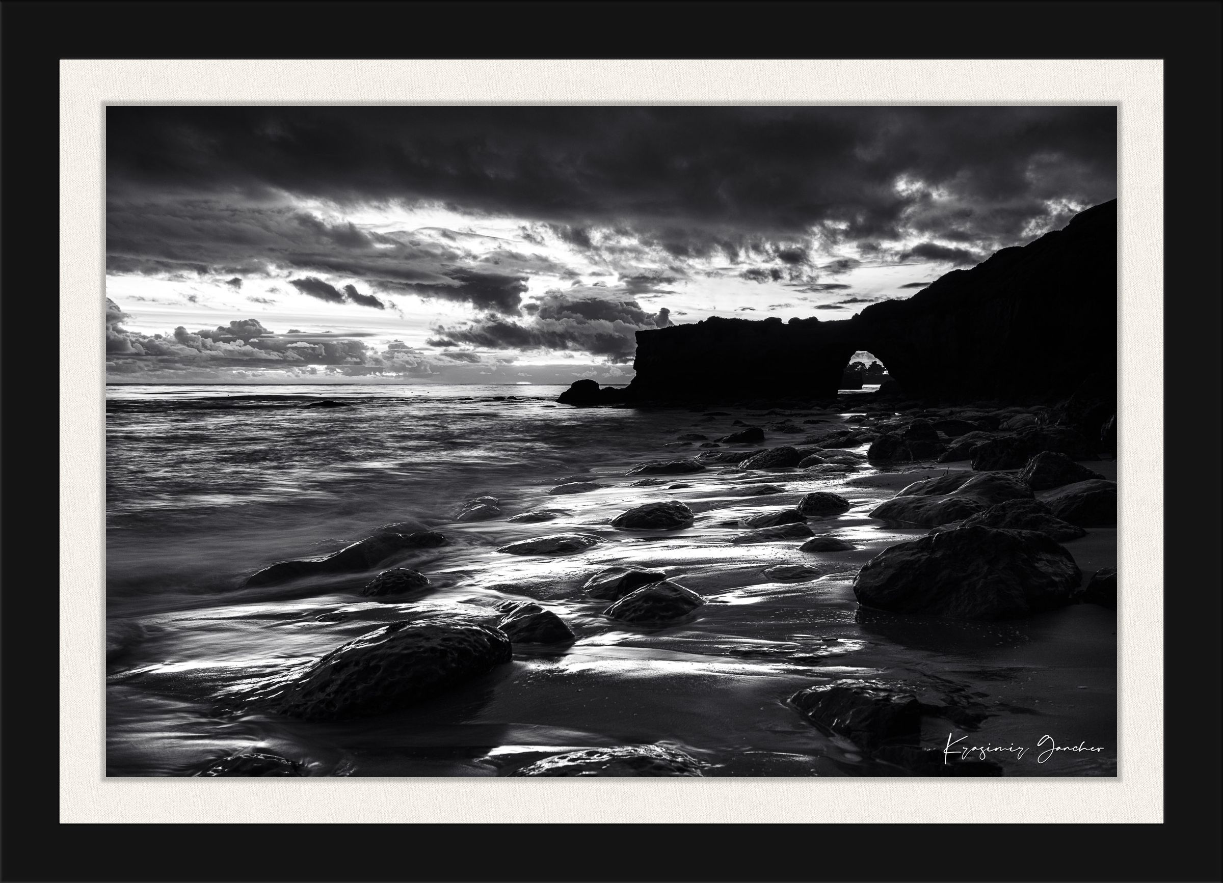 Black-and-white photograph showcasing a rock arch at Santa Cruz’s coastline during sunset with flowing waves. #Finish_Roma Satin Black Frame & Bright Liner
